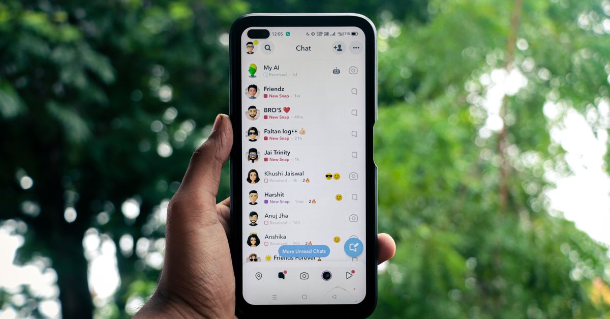 A hand holding a smartphone displaying a chat application outdoors against a green background.